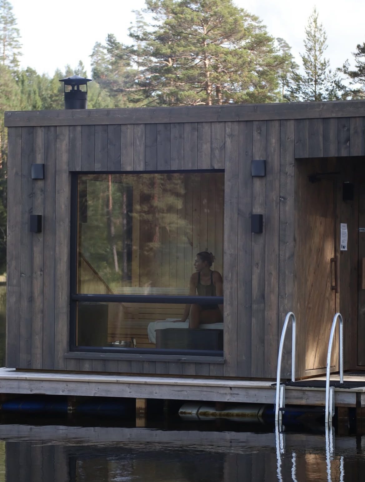 Utsikt gjennom badstuvinduet, med en gjest inne i varmen og stigen ned til vannet.
